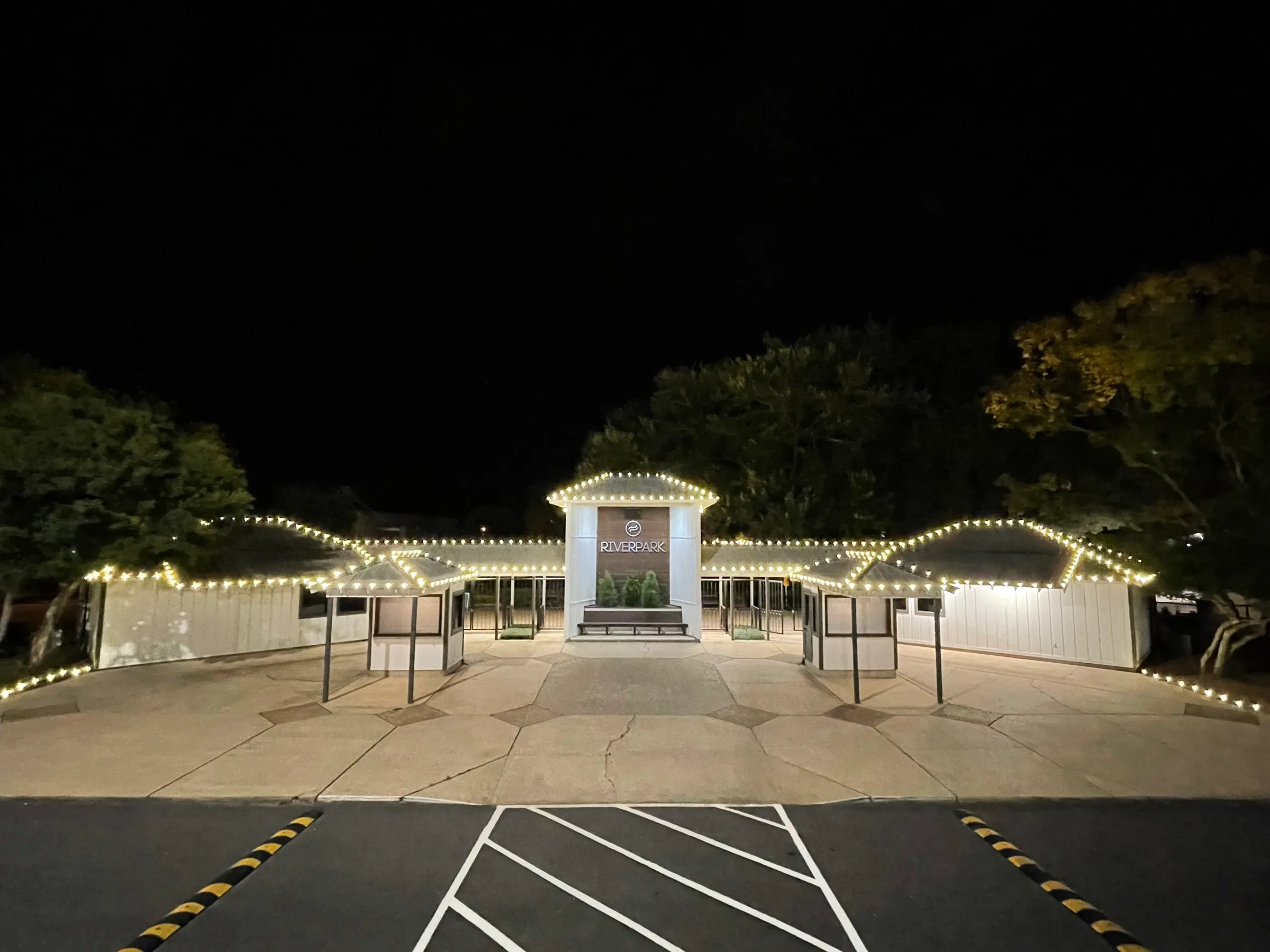 A clubhouse roofline outlined in warm white C9 bulbs at night, with the entrance canopy lit below.
