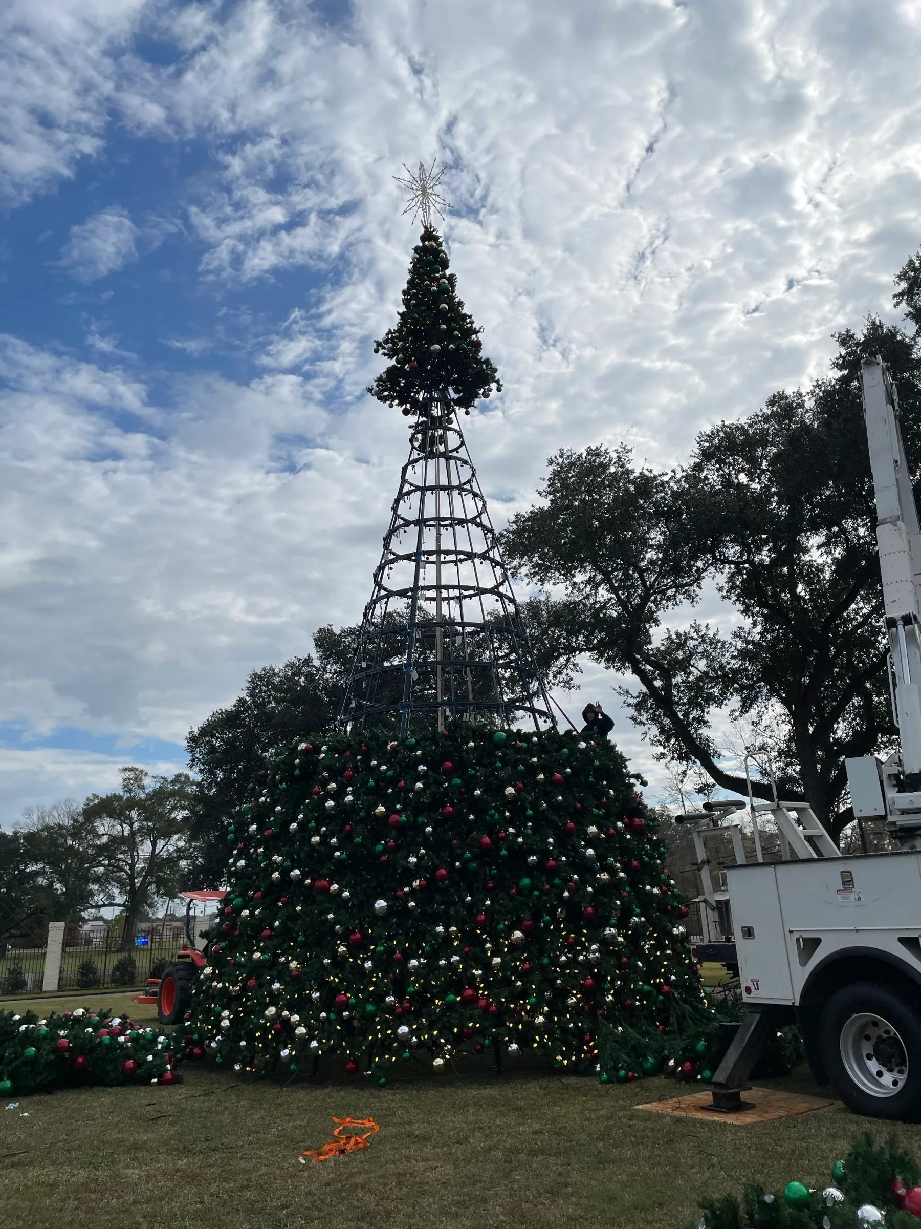 A commercial Christmas tree frame with foliage part way installed, with a bucket truck alongside.