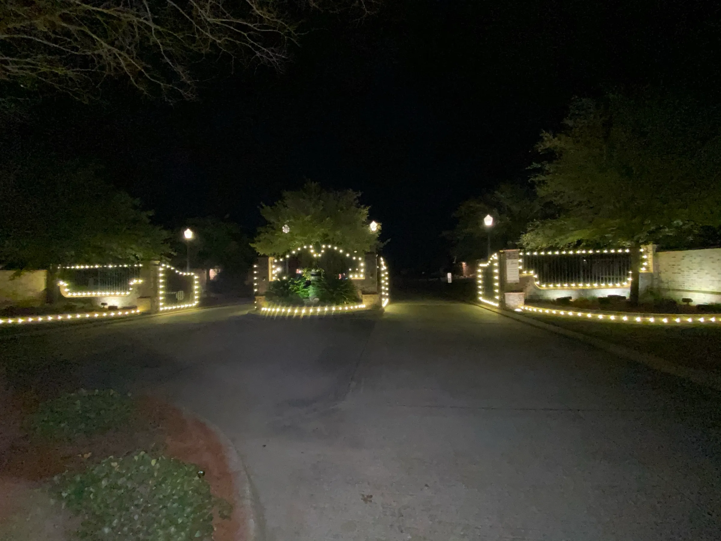 A gated property entrance at night with warm white lighting running along both entry walls.