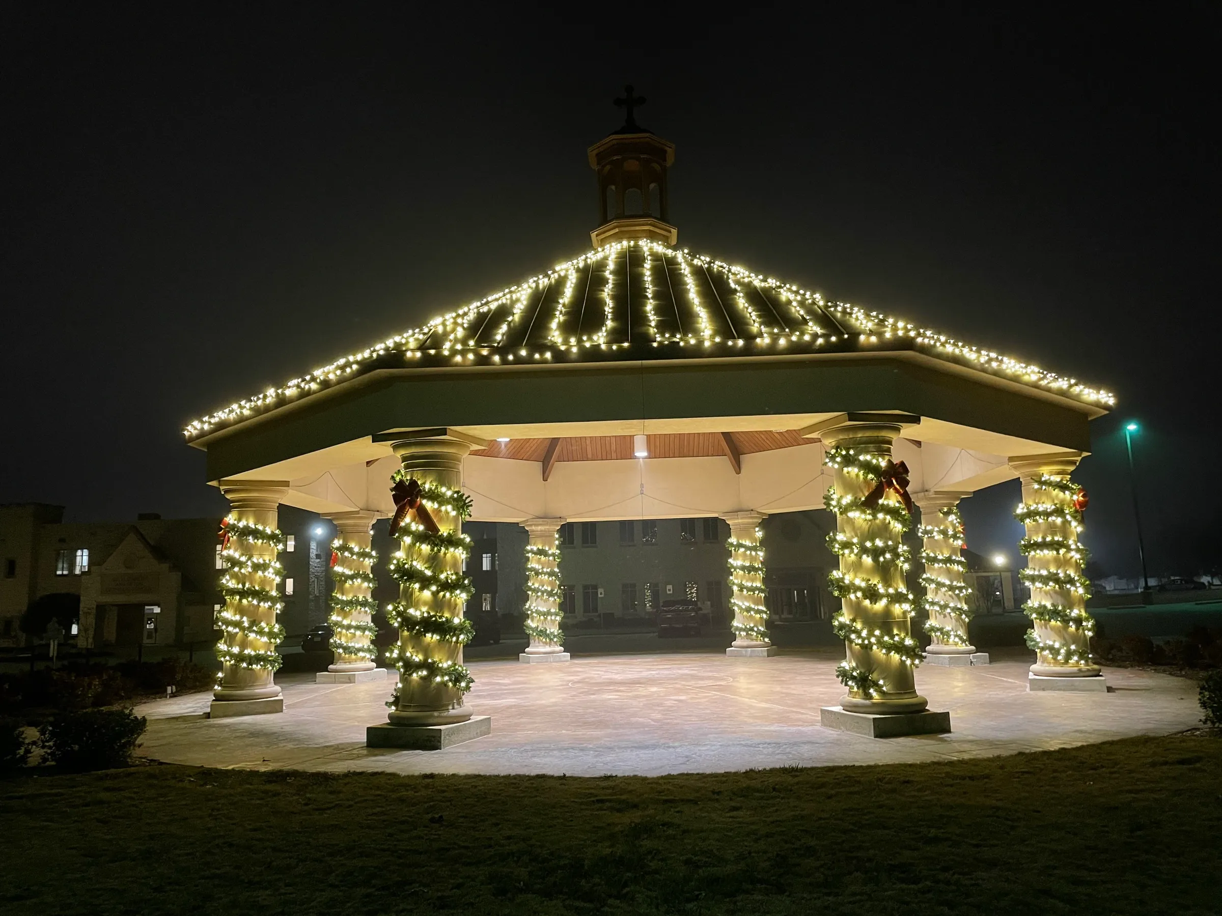 A stone pavilion at night with its roofline outlined in lights and every column wrapped in garland.