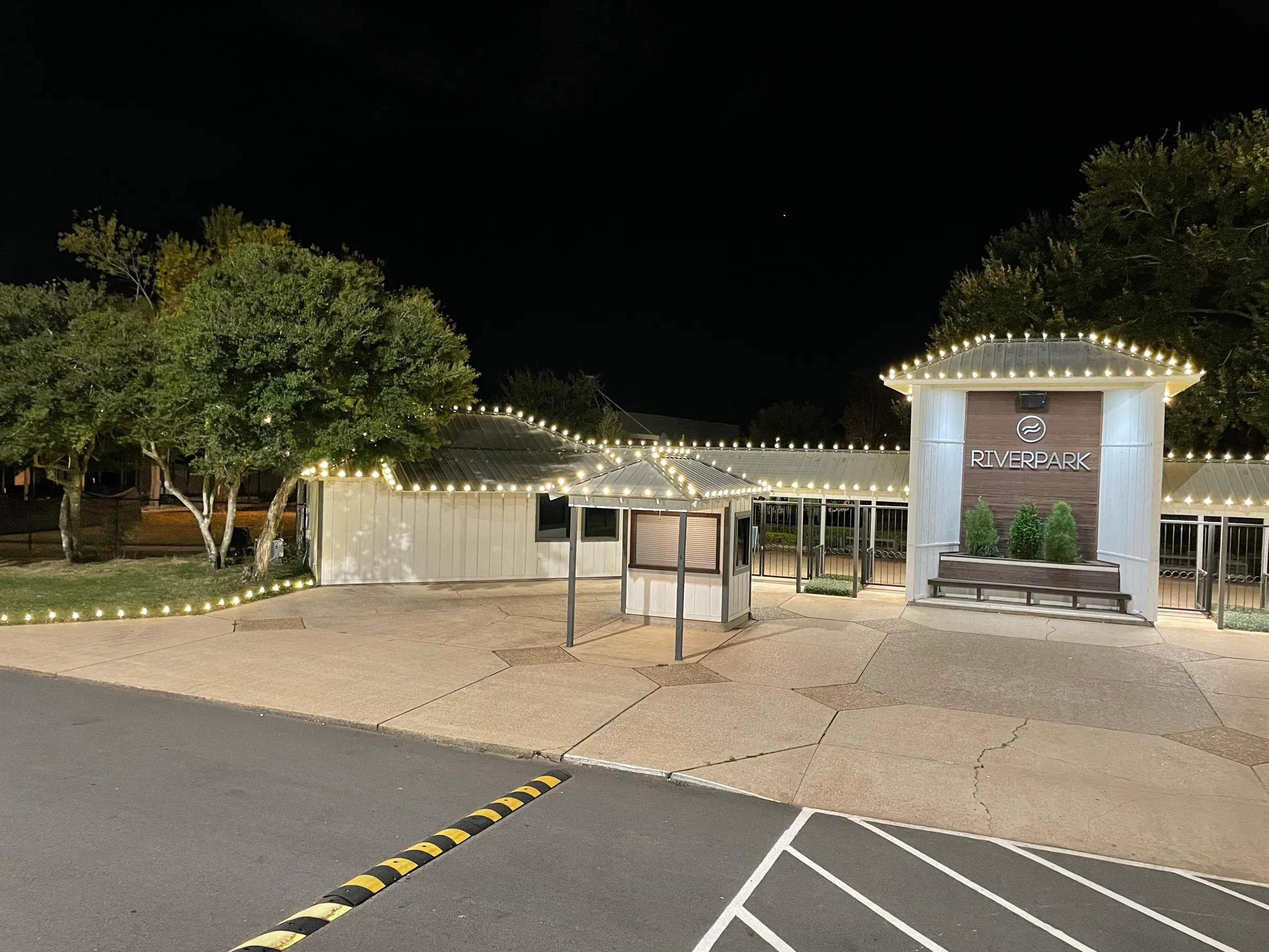 The lit entrance and covered walkway of a clubhouse at night, roofline traced in warm white.