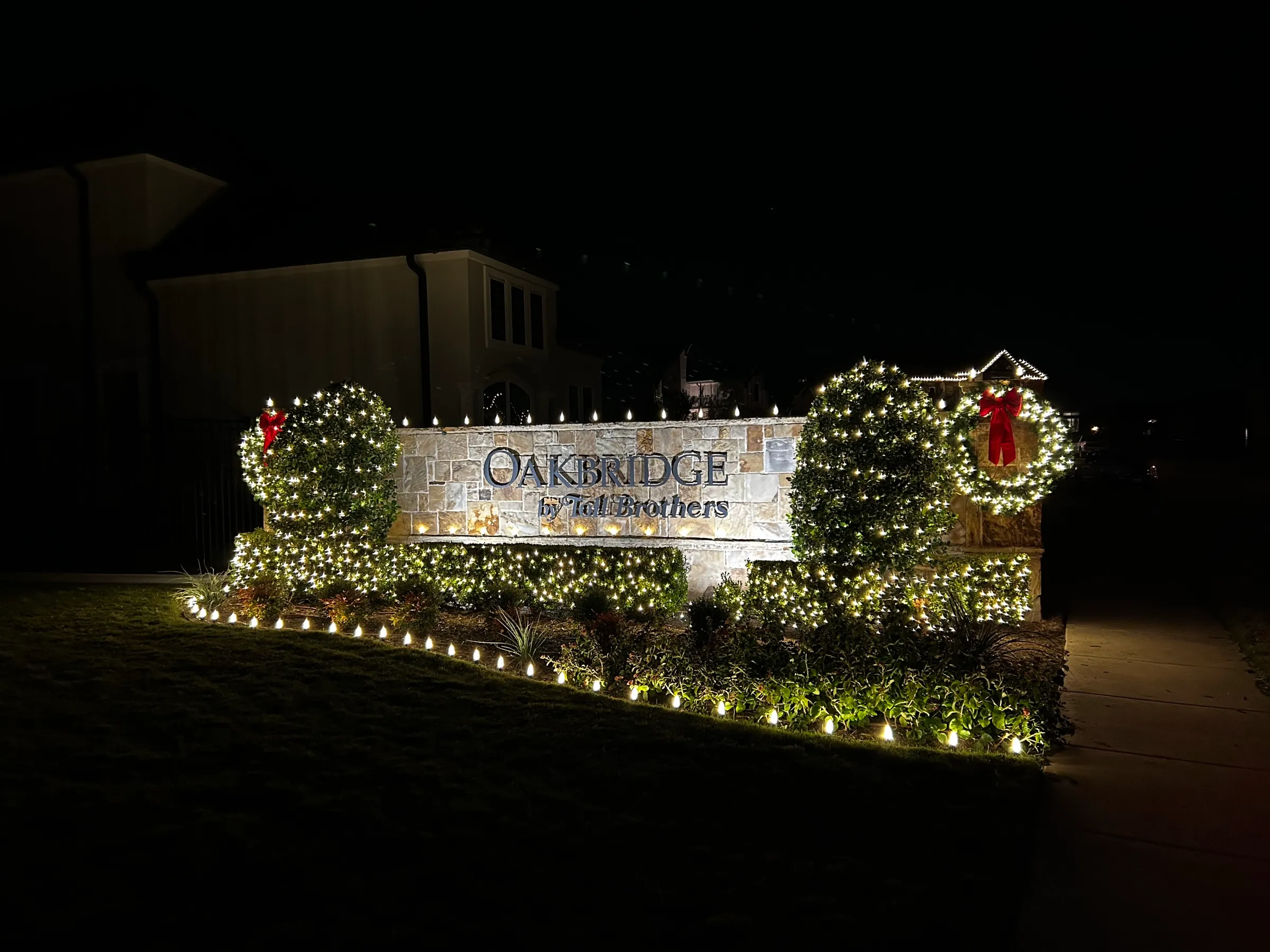 A stone property entry monument at night with lit surrounds and landscape lighting along the beds.