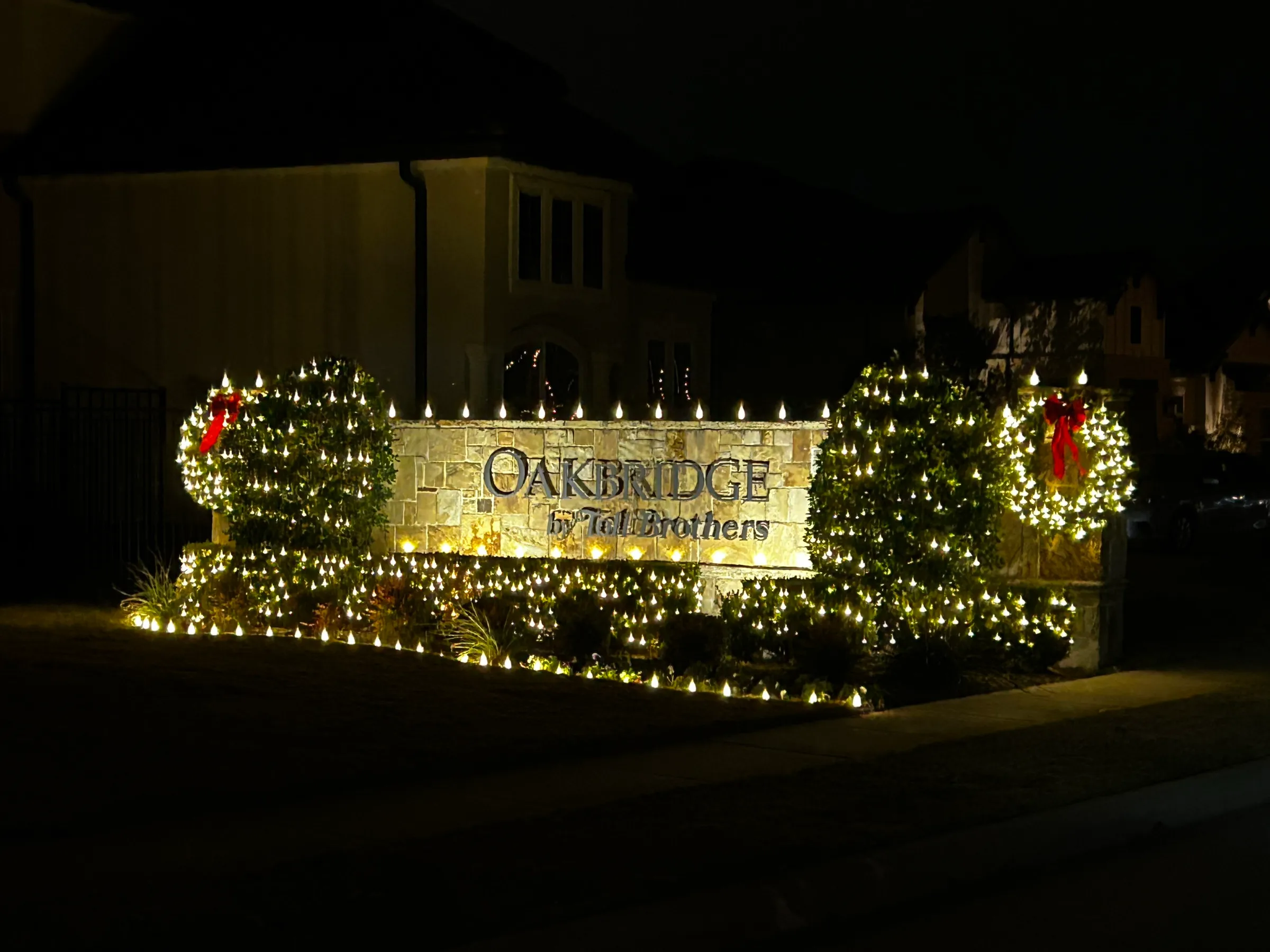 A property entry monument decorated with lit wreaths, garland and red bows at night.