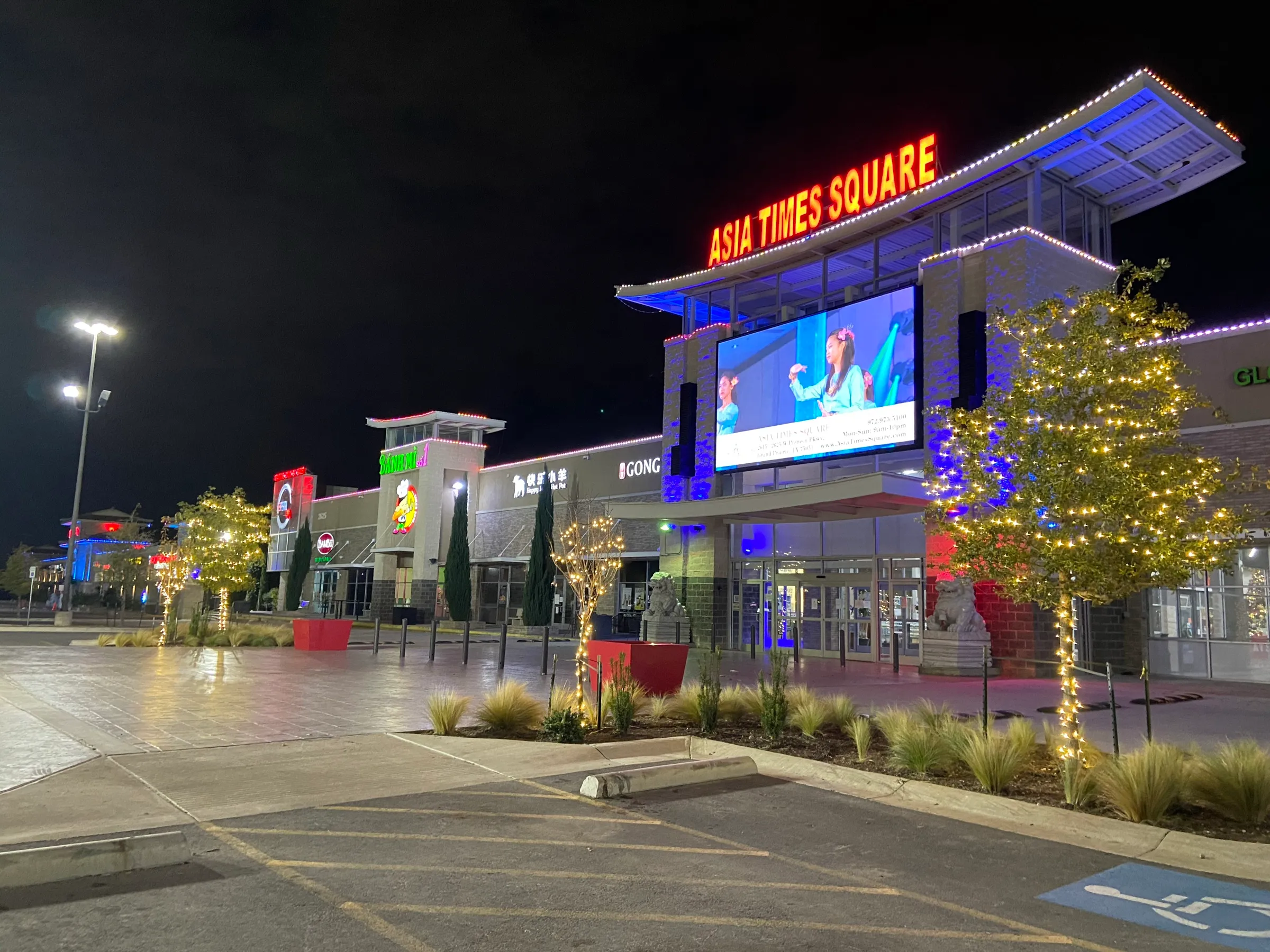 The main entrance of a retail centre at night with wrapped trees framing the walkway.