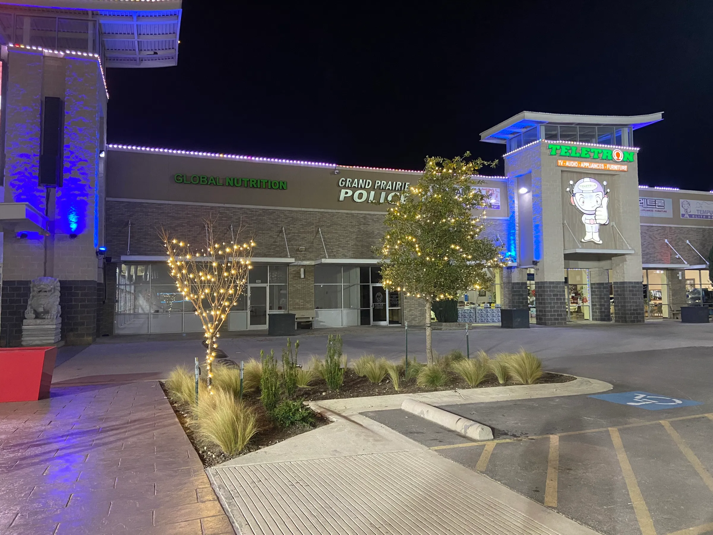 Wide night view of a retail centre facade with wrapped landscape trees along the storefronts.
